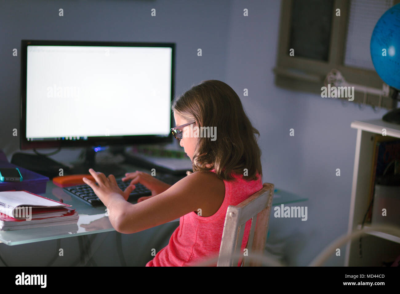 Ragazza giovane seduto alla scrivania, facendo i compiti, tramite il computer Foto Stock