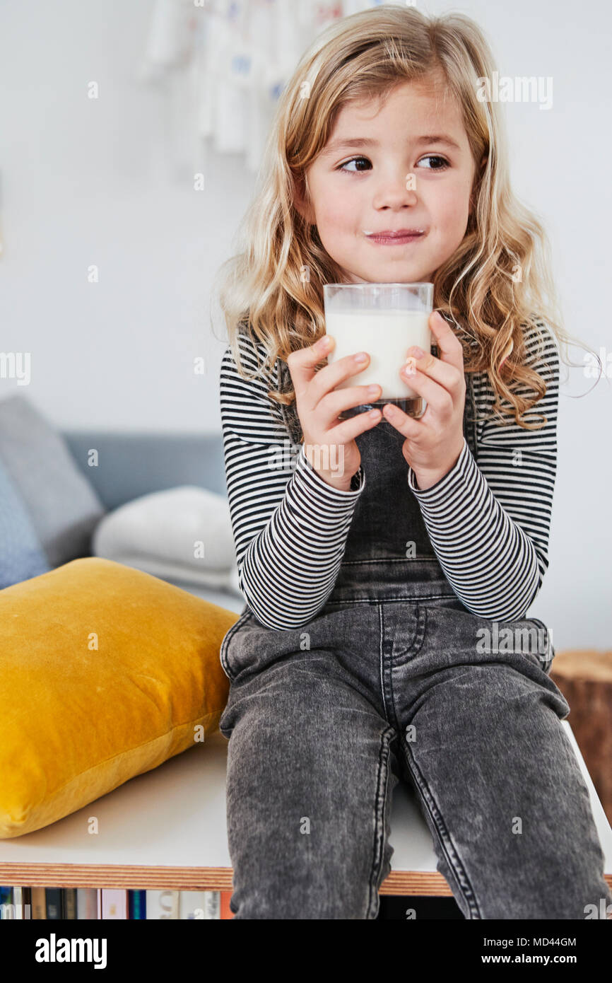 Giovane ragazza seduta nel salotto, tenendo in mano un bicchiere di latte Foto Stock
