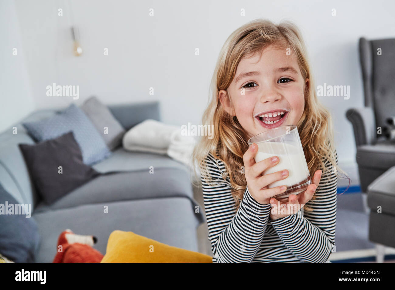 Ritratto di giovane ragazza seduta nel salotto, tenendo in mano un bicchiere di latte, sorridente Foto Stock