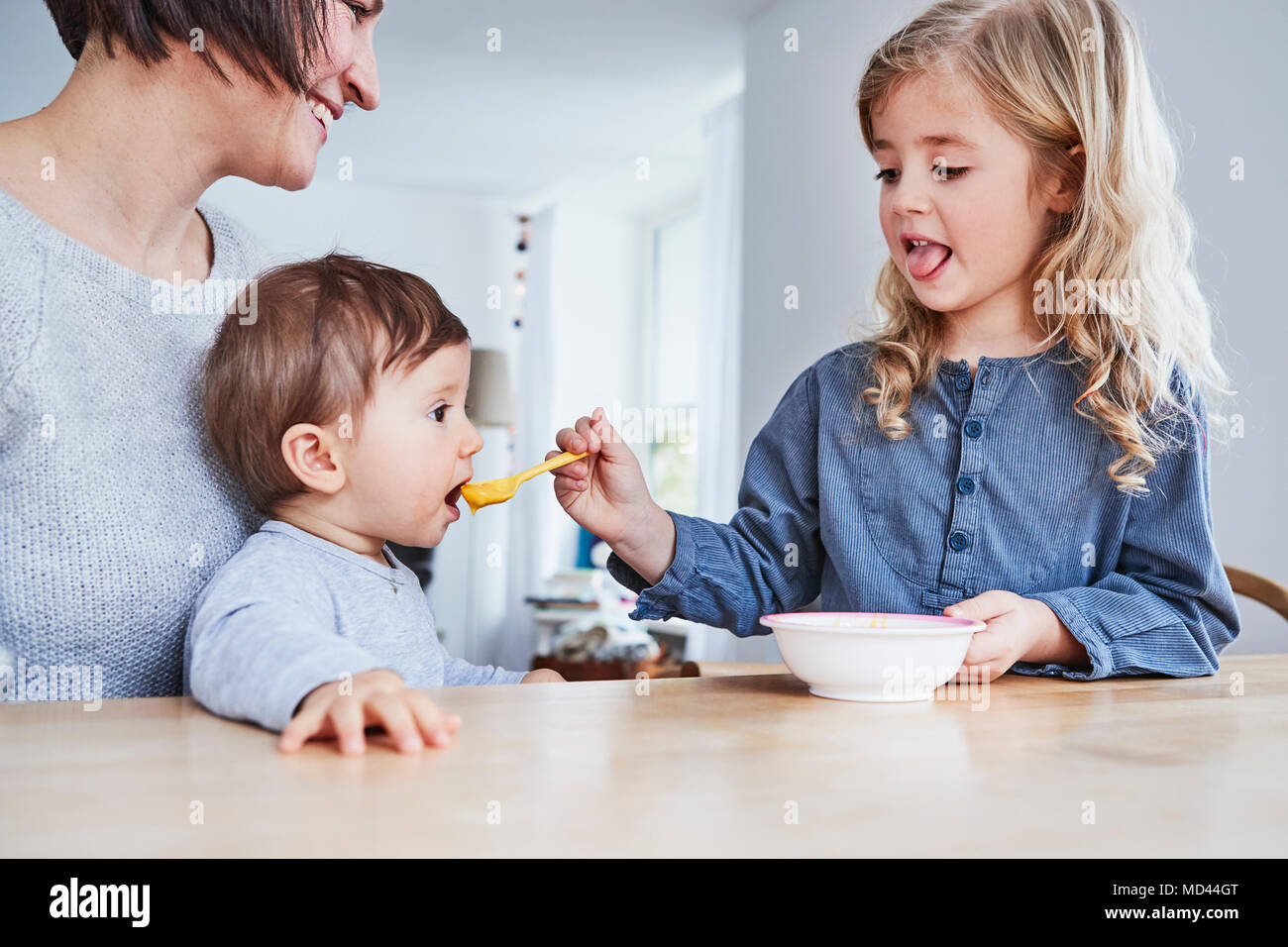 Famiglia seduti al tavolo da cucina, giovane ragazza spoon-alimentazione la sorella del bambino Foto Stock