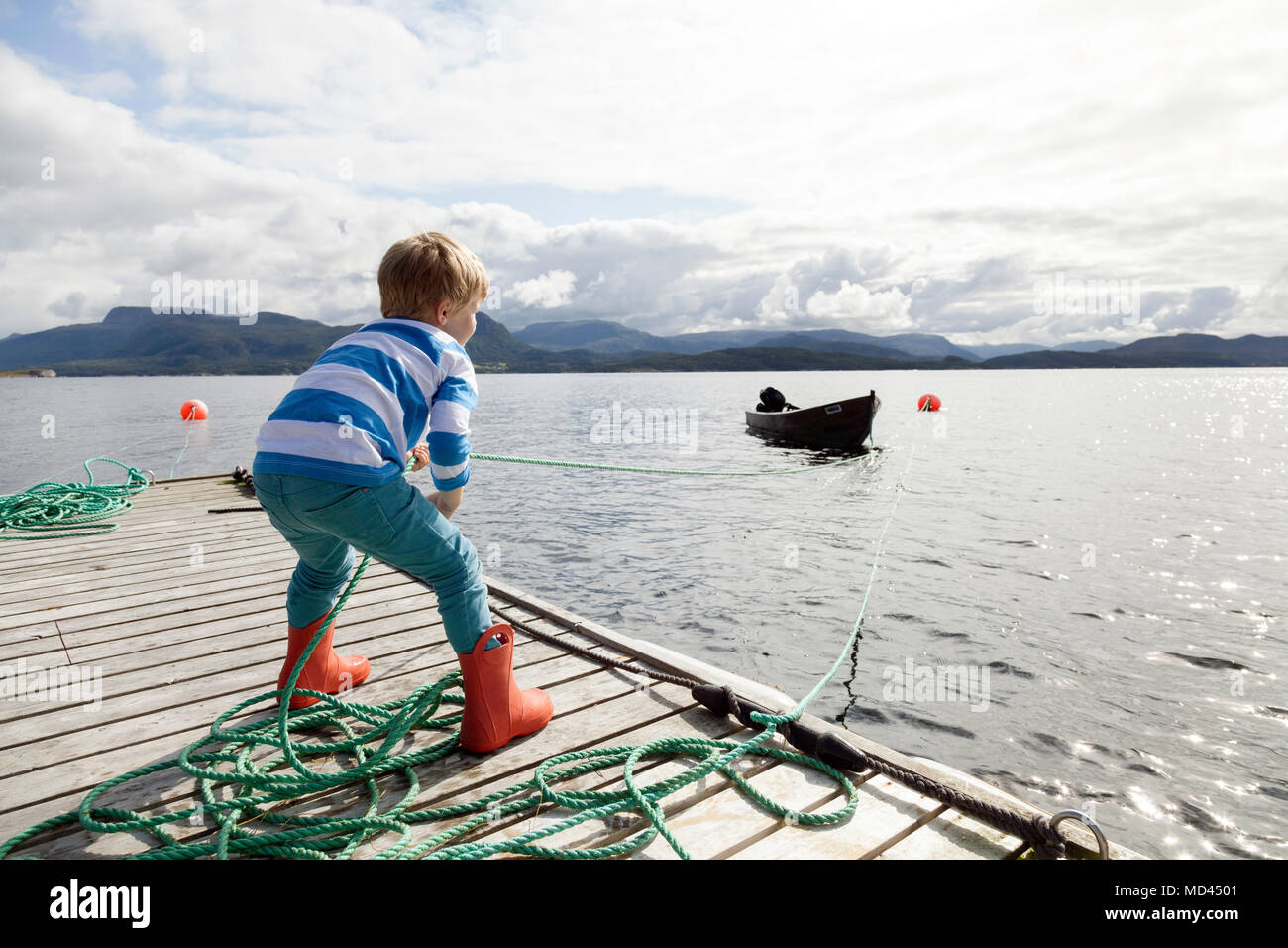 Ragazzo sul molo tirando fjord barca da corda, Aure, More og Romsdal, Norvegia Foto Stock