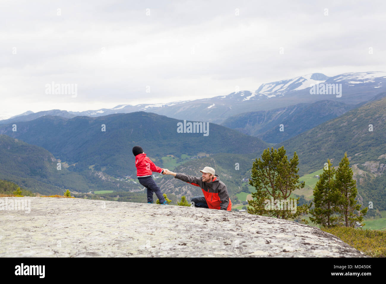 Ragazzo aiutando escursionista padre su roccia nel paesaggio di montagna, parco nazionale di Jotunheimen, Lom, Oppland, Norvegia Foto Stock