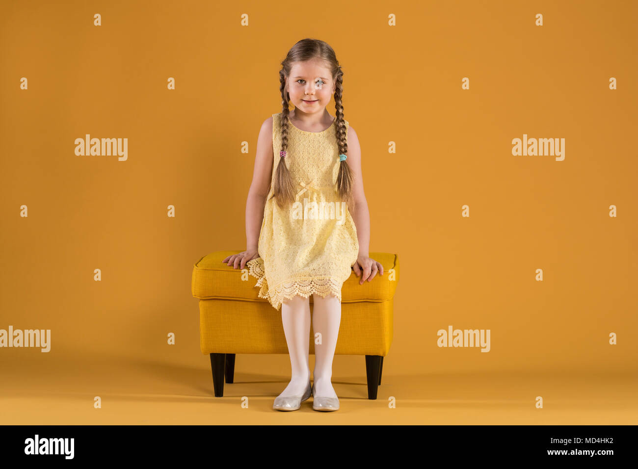 Ritratto pieno di giovani felici ragazza seduta sul pouf giallo Foto Stock