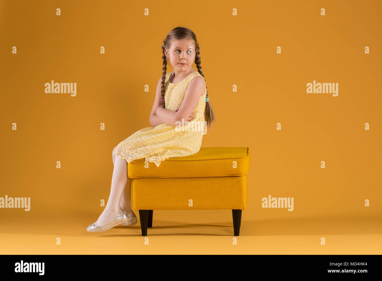 Ritratto di giovane ragazza in abito giallo seduta sul pouf con bracci incrociati Foto Stock