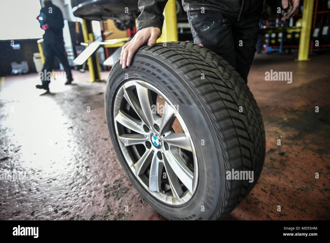 Un meccanico di rotoli di un auto pneumatico sul pavimento del garage Foto Stock