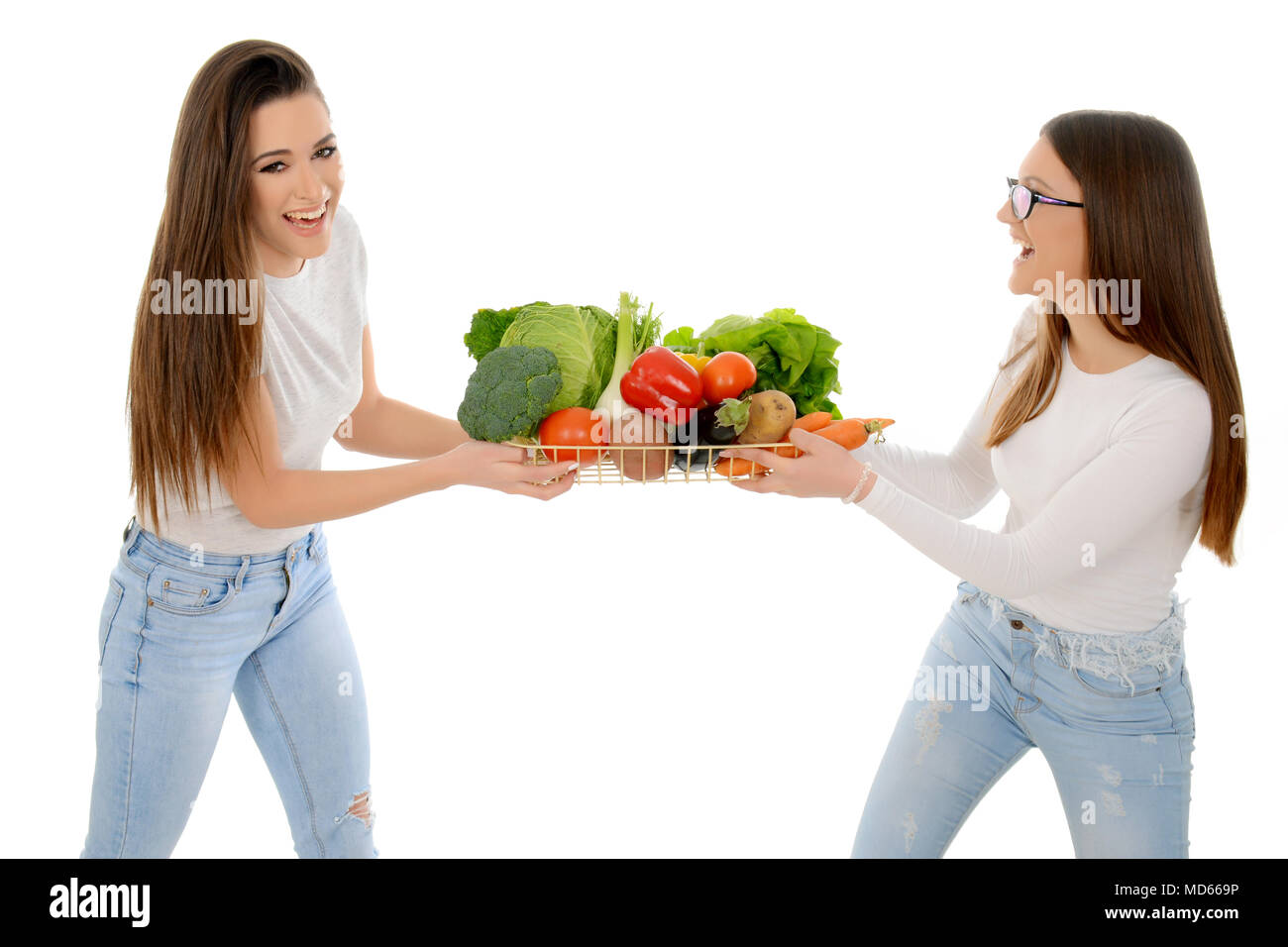 Due ragazze ridere per scramble cesto pieno di verdure miste Foto Stock