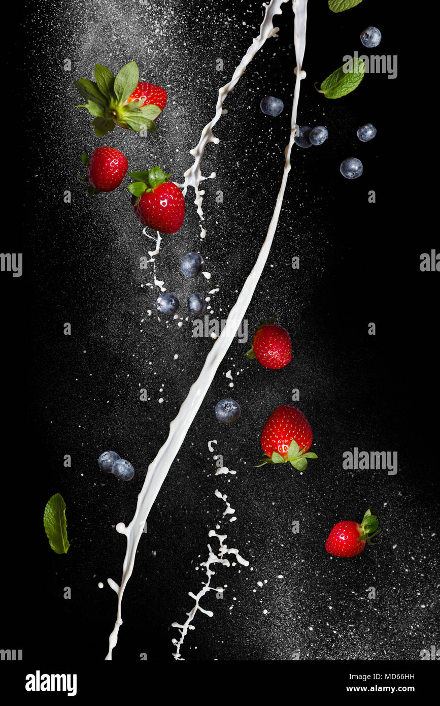 Berry mix. Fresche fragole mature e mirtilli in volo su uno sfondo nero. Flussi a spirale di latte Foto Stock