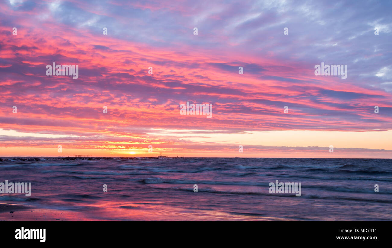 Incredibili nuvole rosso colorato dal tramonto sul mare calmo e una silhouette di una lontana mole. Foto Stock