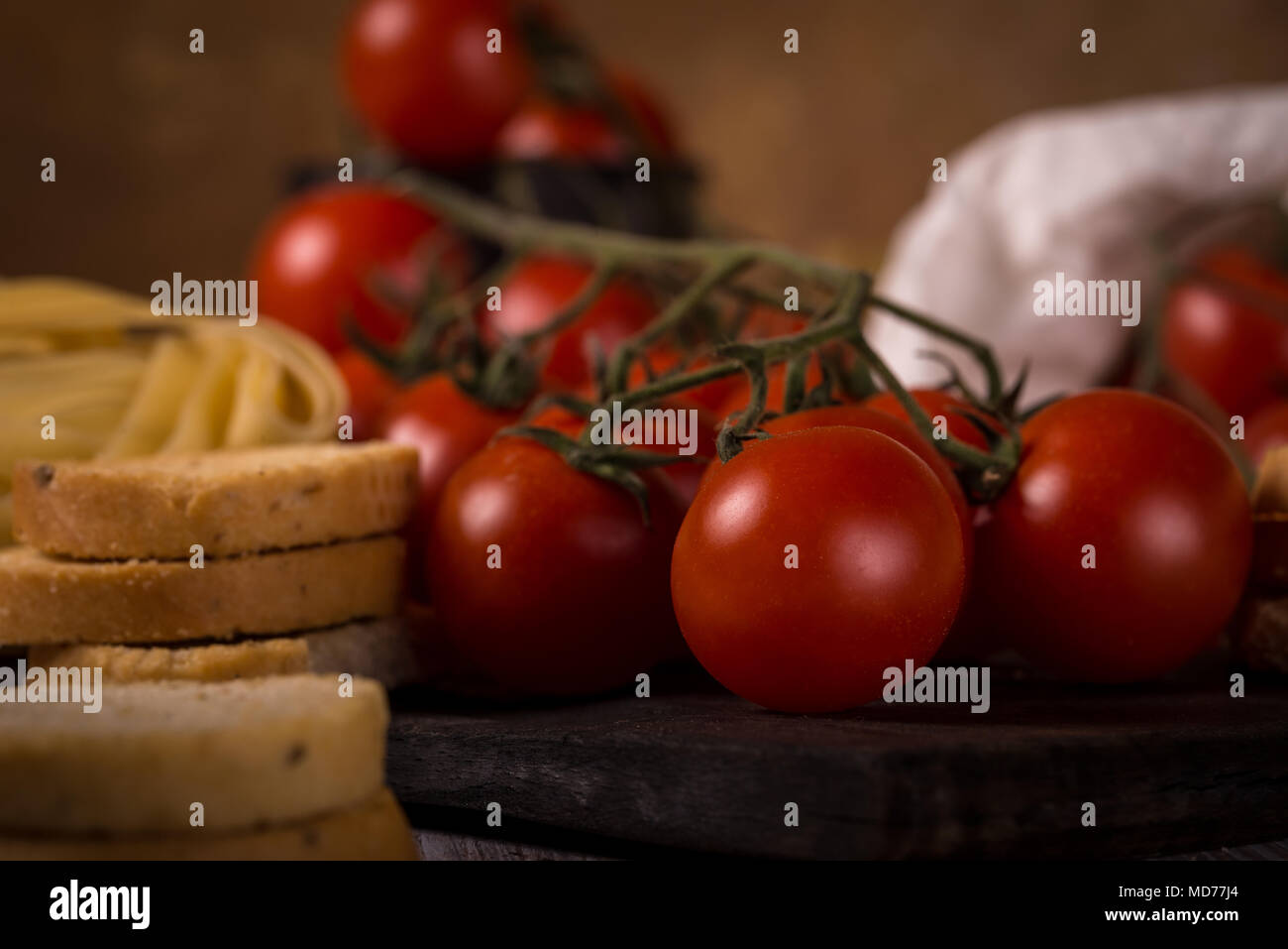 Foto orizzontale con ramoscello pieno di rossi pomodori ciliegini collocato su indossato tavola di legno con le tagliatelle e alcuni pezzi di bruschetta all'aglio anelli. Accanto a Foto Stock