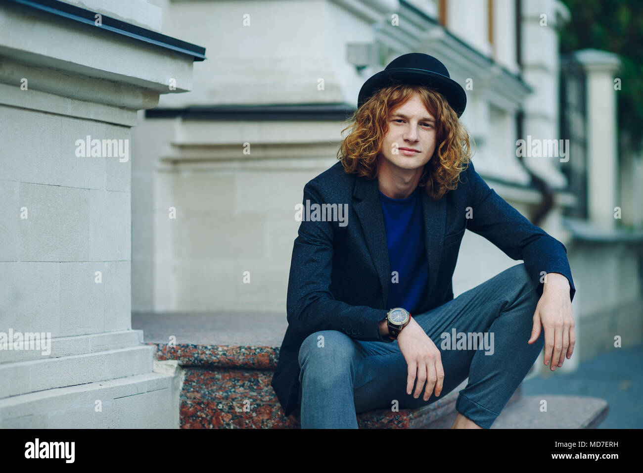 Moda Ritratto di giovane uomo rossiccio con lunghi capelli ricci seduti  sulle scale. Uomo bello indossando un cappello. Awesome persone concetto  Foto stock - Alamy