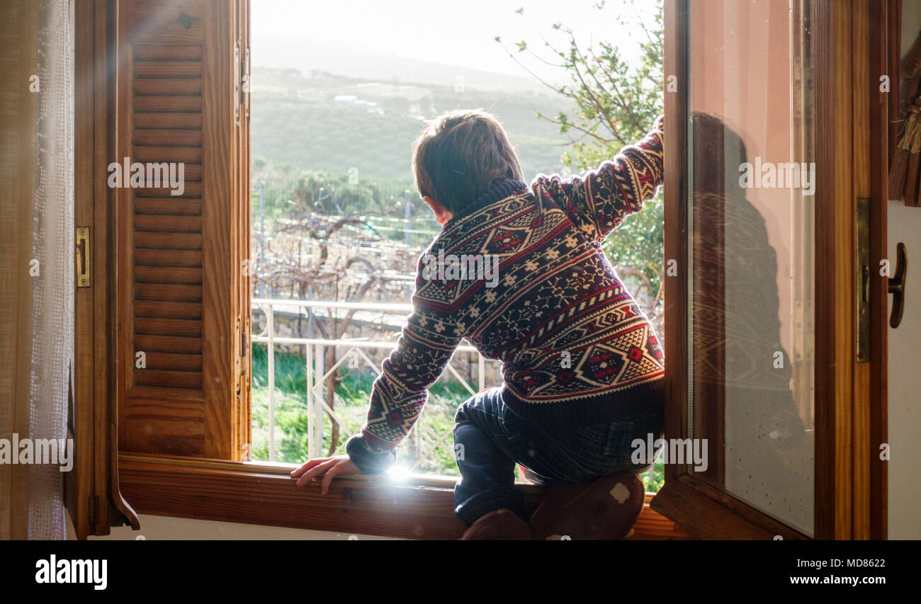 Vista posteriore del ragazzo seduto sulla finestra della casa, Grecia Foto Stock