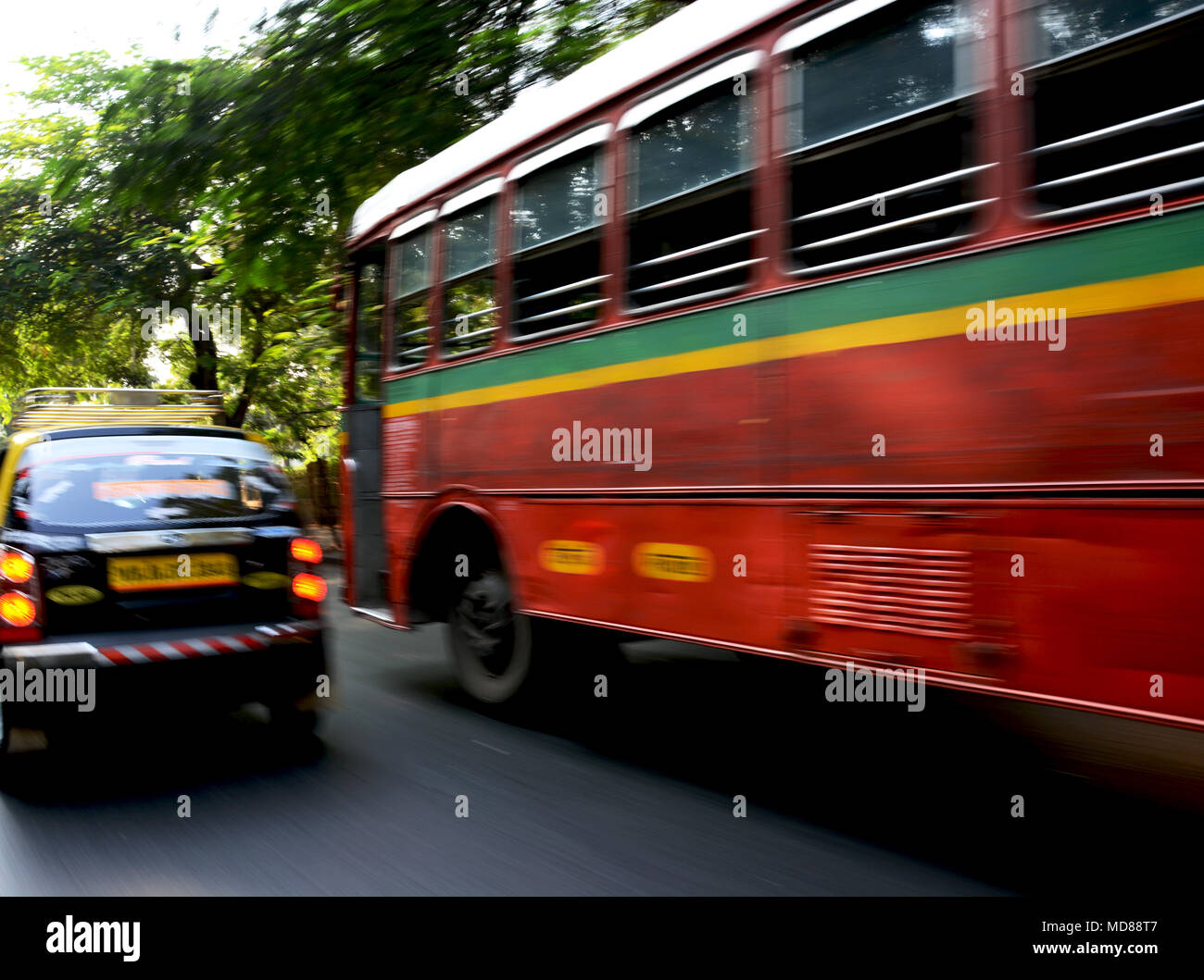 Un rosso Ashok Leyland Bus e taxi lo zoom a fianco di ciascun altro attraverso il traffico di Mumbai, India Foto Stock