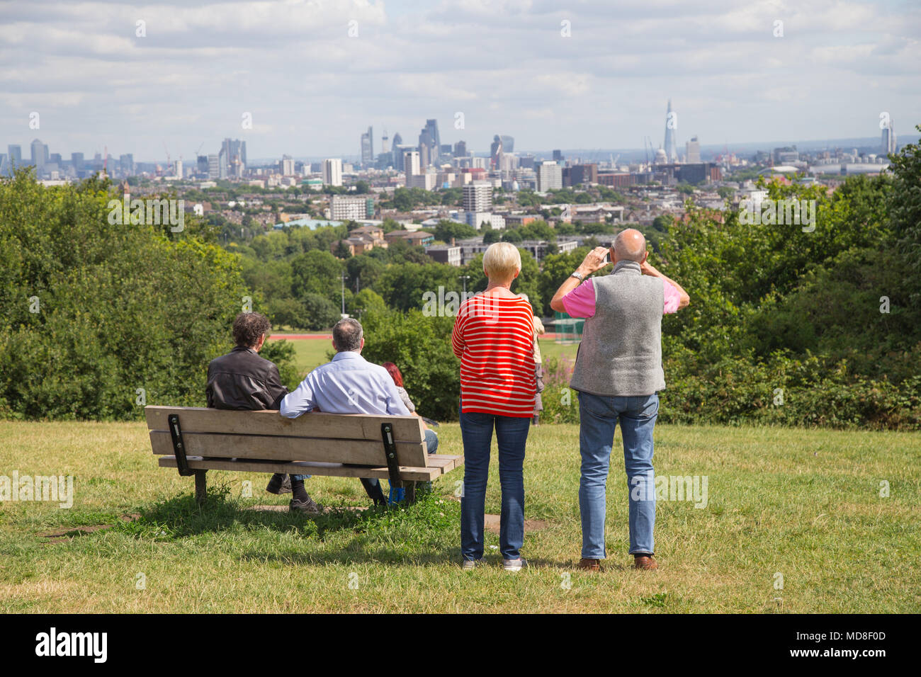 Persone di mezza età rilassarsi e godere della vista panoramica della skyline di Londra un pomeriggio estivo sulla Collina del Parlamento, Hampstead Heath, a nord di Londra Foto Stock