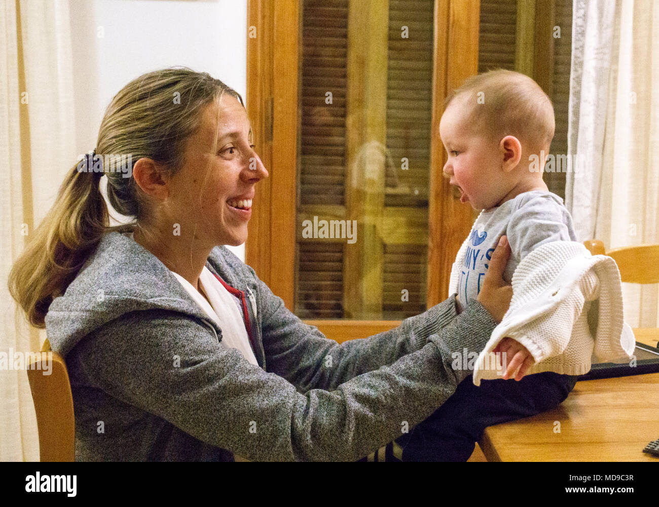 Madre sorridente al bambino seduto su un tavolo, Grecia Foto Stock