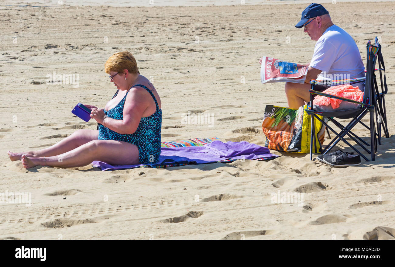 Bournemouth Dorset, Regno Unito. Il 19 aprile 2018. Regno Unito: meteo bella calda giornata di sole a Bournemouth spiagge con cielo azzurro e sole ininterrotta, come i visitatori in testa al mare per godere il giorno più caldo dell'anno finora. Coppia matura a rilassarci in spiaggia, donna sms sul cellulare mentre l uomo legge giornale. Credito: Carolyn Jenkins/Alamy Live News Foto Stock