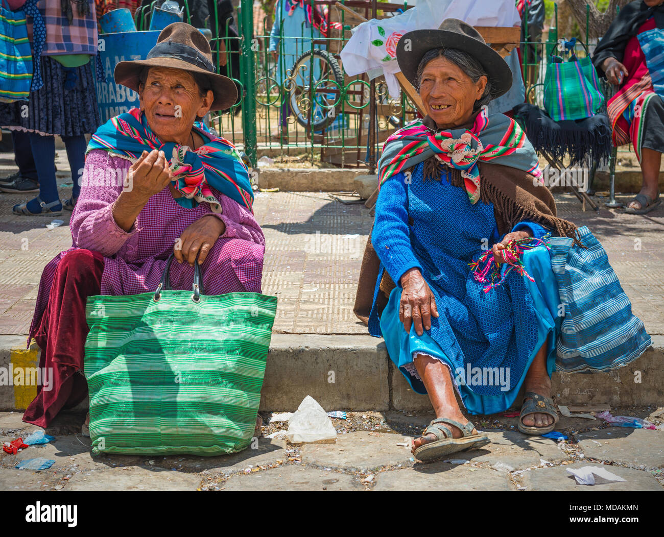 Due senior donne indigene del Tarabuco minoranze indigene in chat e parlare, seduto sul marciapiede, sul mercato di domenica, Tarabuco, Bolivia Foto Stock
