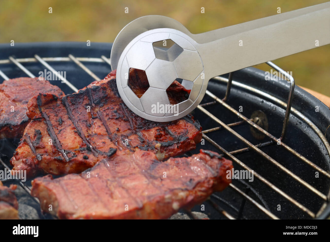 Close up di gustose bistecche sul barbecue grill con la Coppa del Mondo di Calcio tong Foto Stock