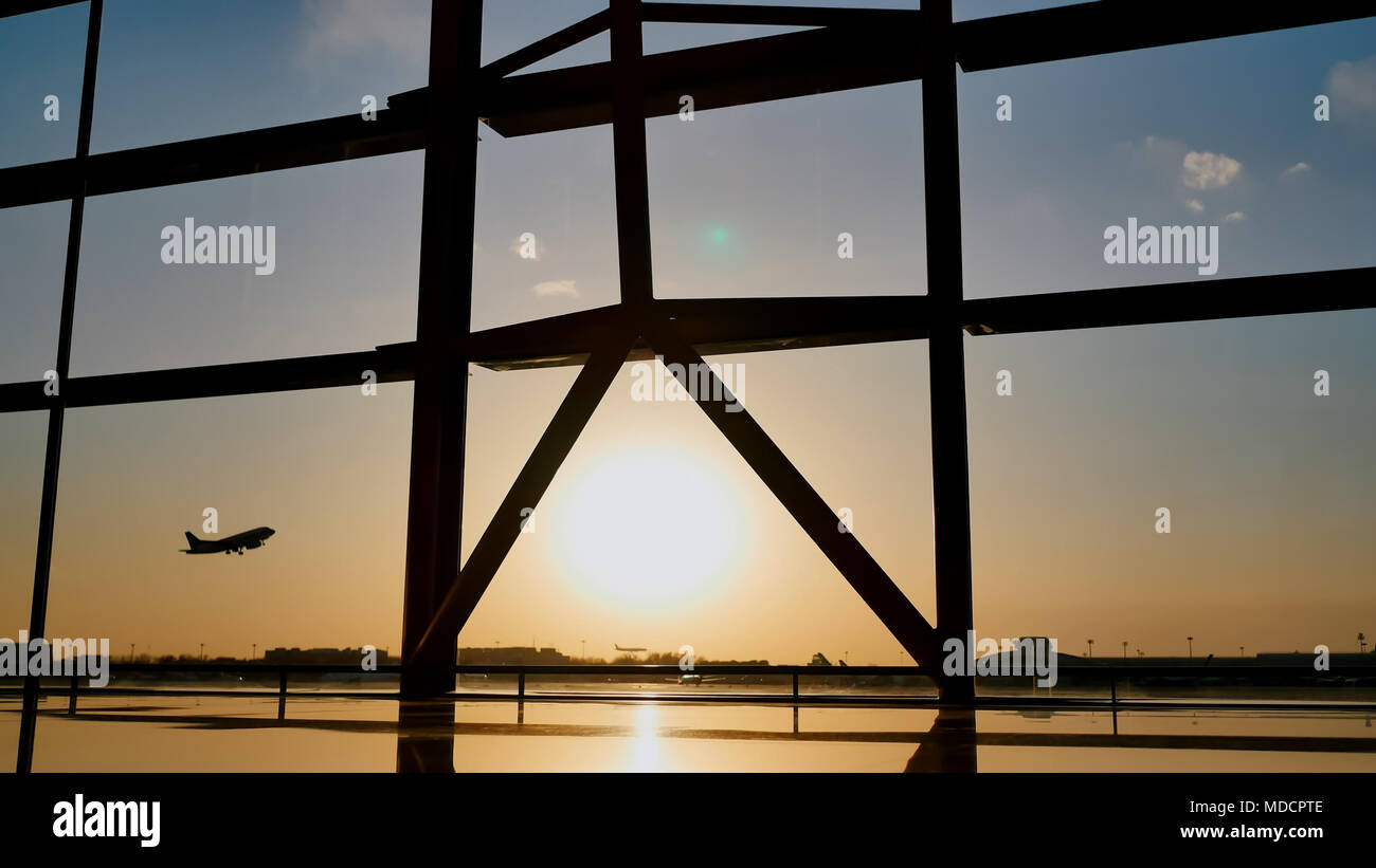 Silhouette di un aereo in fase di decollo al tramonto all'aeroporto di Pechino sullo sfondo di una finestra. Foto Stock