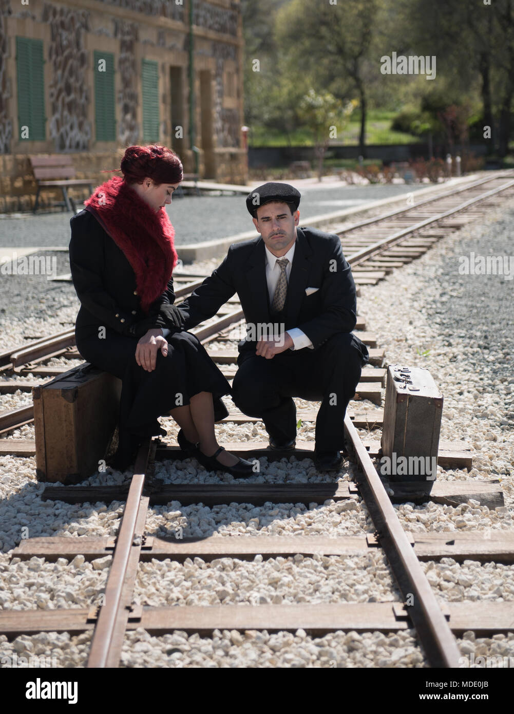 Coppia giovane con valigia vintage in pensieri profondi ubicazione sul trainlines attesa per il prossimo treno pronto per la separazione. Foto Stock