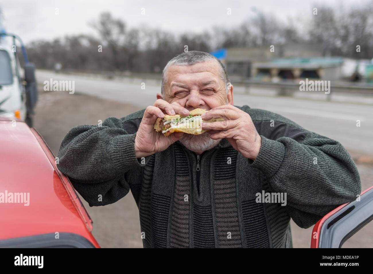 Ritratto di caucasici driver senior mangiare lyulya kebab in lavash vicino la sua auto Foto Stock