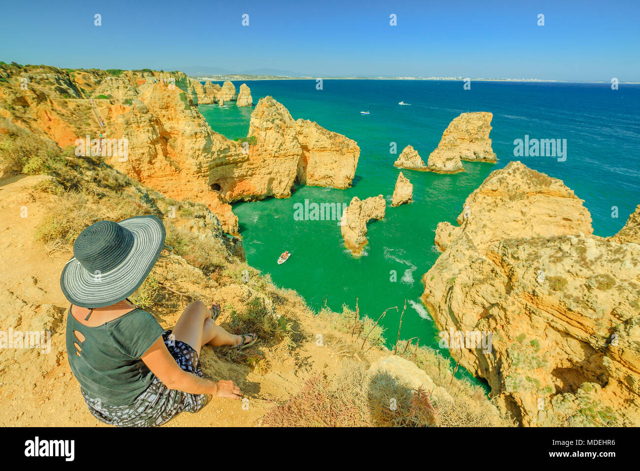 Vacanze estive in Algarve, Portogallo. Stile di vita turistico con hat seduti sul promontorio di Ponta da Piedade e si affaccia sulla costa di Lagos con iconico scogliere calcaree e. Il mare turchese, giornata di sole. Foto Stock