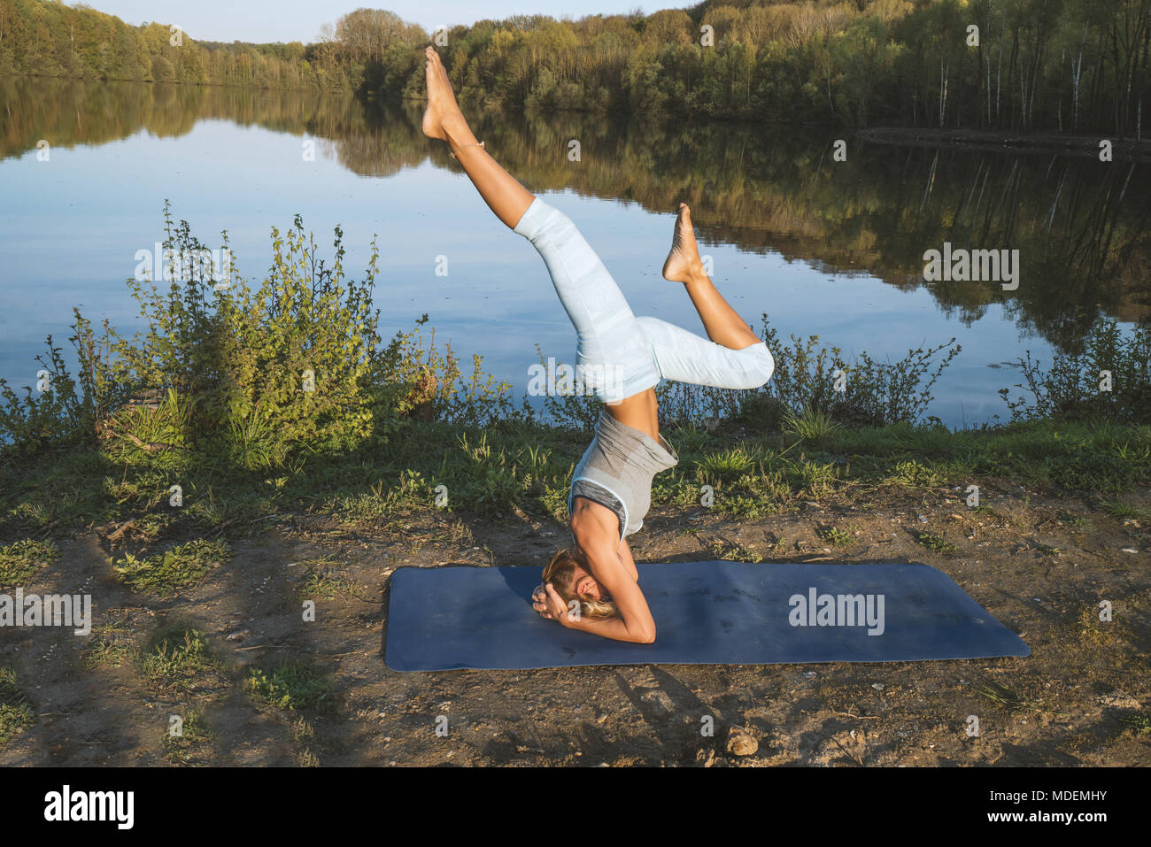 Giovane donna esercizio di yoga in riva al lago al tramonto, persone Viaggi natura benessere e relax concetto. Girato in Francia, l'Europa. Headstand pongono Foto Stock