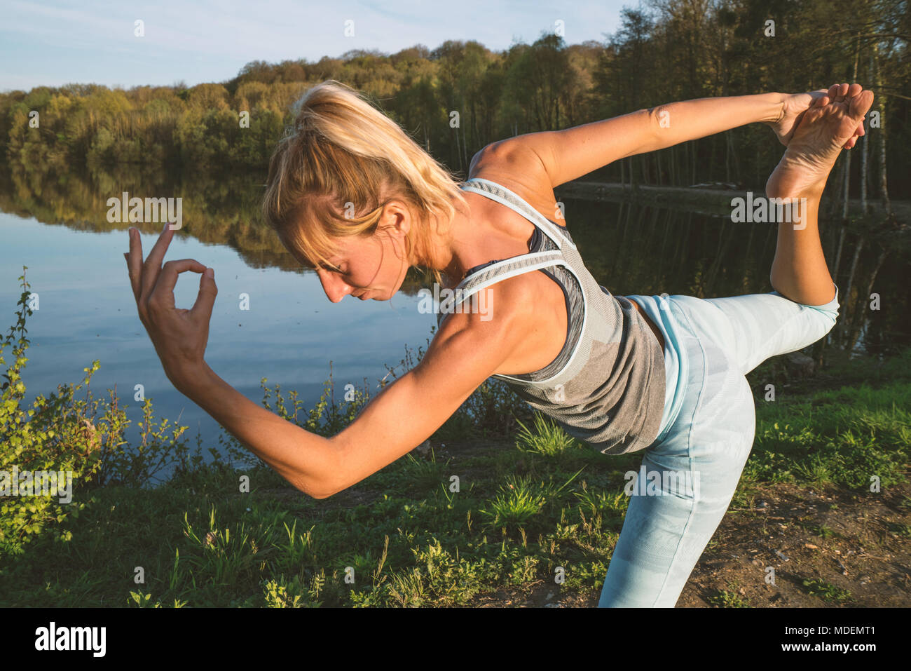 Giovane donna esercizio di yoga in riva al lago al tramonto, persone Viaggi natura benessere e relax concetto. Girato in Francia, l'Europa. Posizione del signore della danza Foto Stock