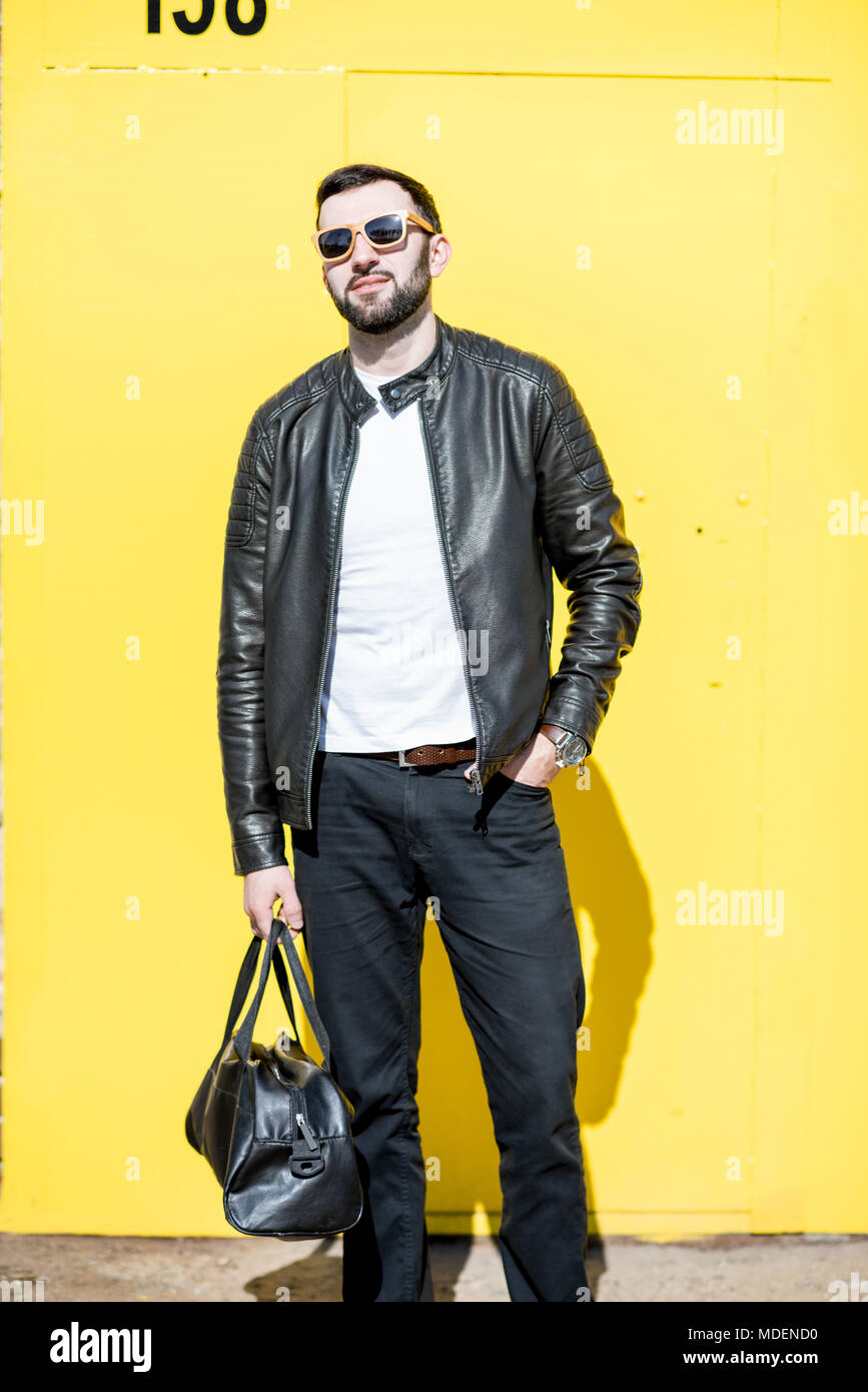 Ritratto di uomo elegante in giacca di pelle con borsa su sfondo giallo  all'aperto Foto stock - Alamy