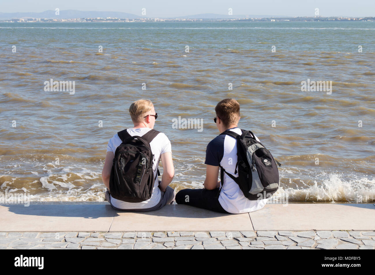 Giovani uomini seduti sul fiume Tago. Lisbona, Portogallo Foto Stock