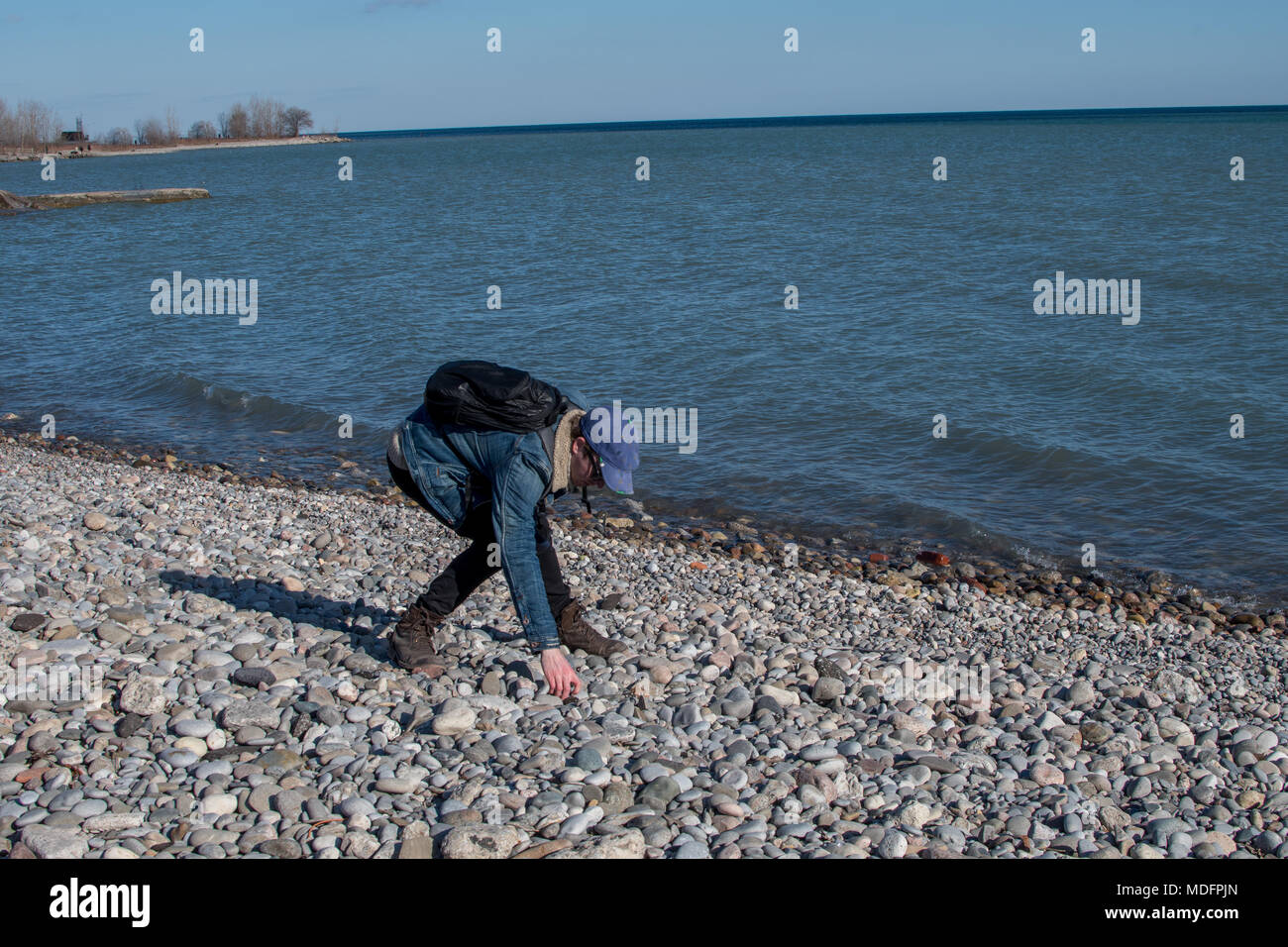 Uomo in piedi sulla spiaggia di raccogliere ciottoli, Toronto, Ontario, Canada Foto Stock