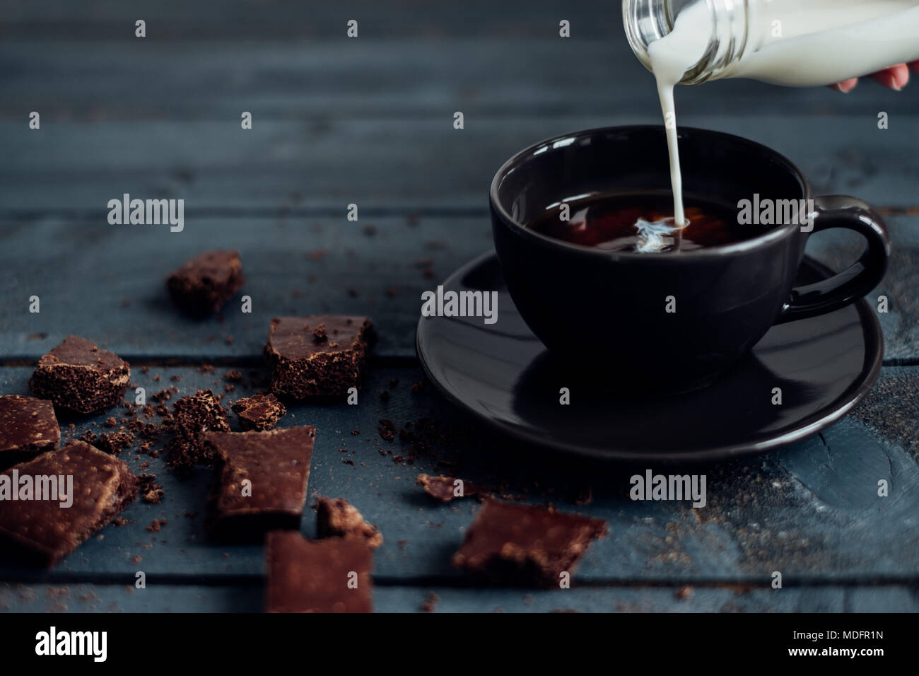 Mano versando il latte in una tazza di caffè con cioccolato fondente Foto Stock