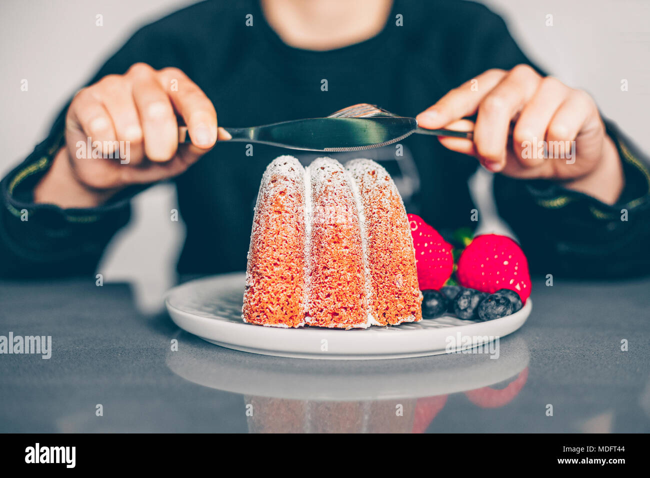Ragazzo seduto a tavola per mangiare una torta con frutta fresca Foto Stock