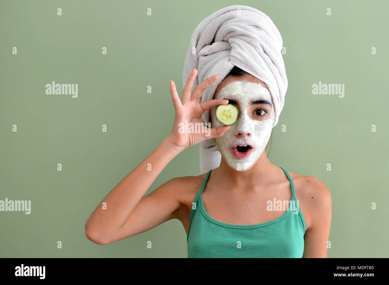 Ragazza con una maschera facciale su tenendo un cucumber slice nella parte anteriore di un occhio Foto Stock