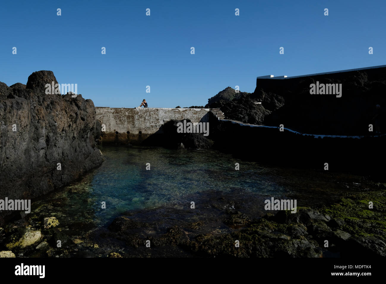 Donna seduta su un muro da piscine naturali, Garachico, Tenerife, Isole Canarie, Spagna Foto Stock