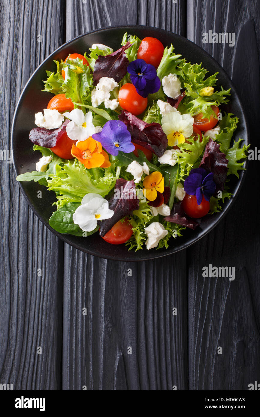 Fresca insalata di organico da fiori commestibili con lattuga, pomodori e crema di formaggio vicino sul tavolo. Verticale in alto vista da sopra Foto Stock