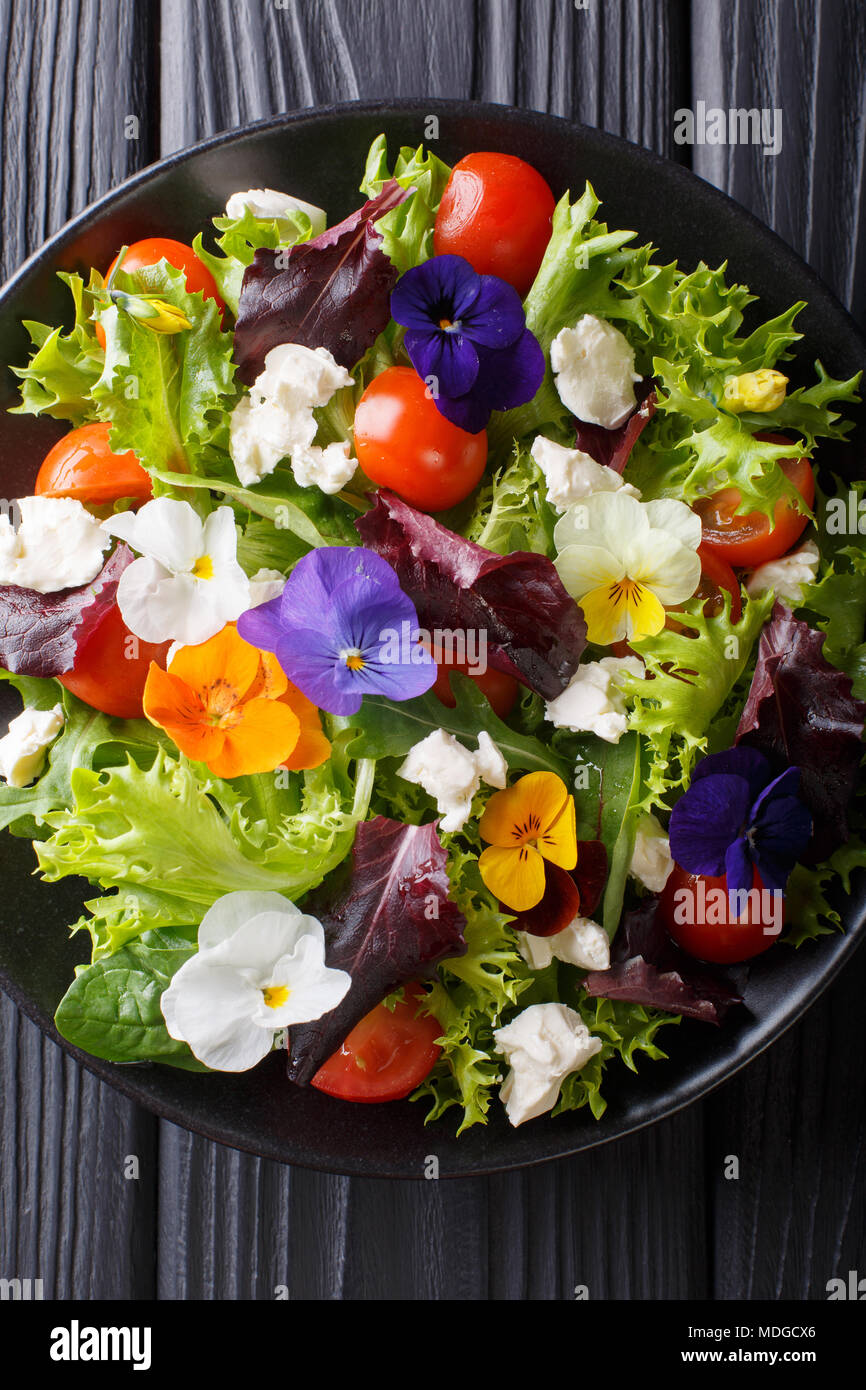 Porzione di insalata con fiori commestibili con lattuga fresca, spinaci, pomodori e formaggio close-up su una piastra. Verticale in alto vista da sopra Foto Stock