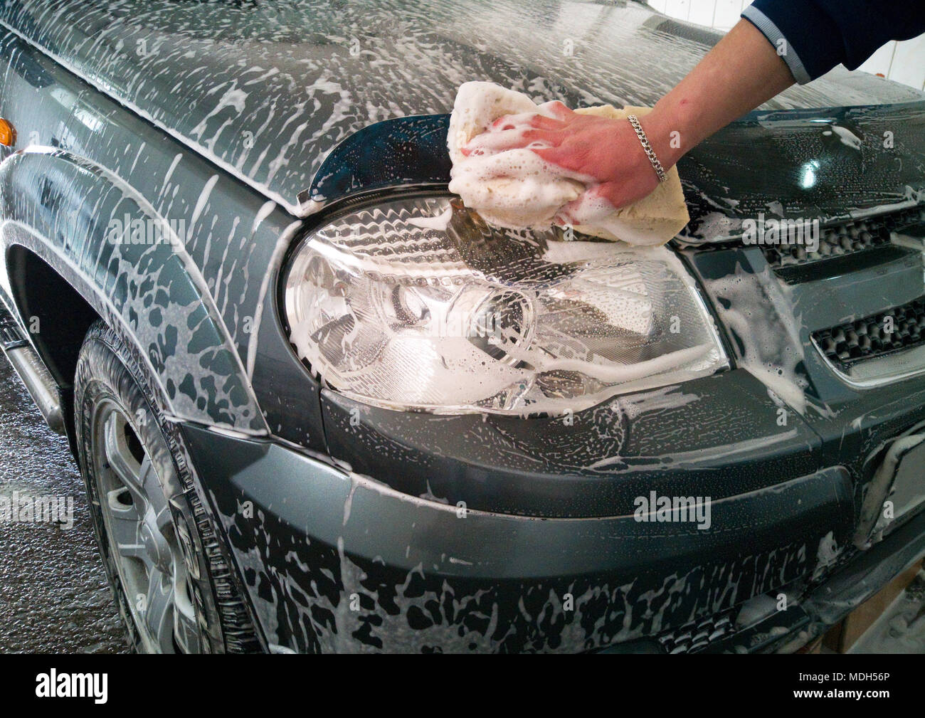 Car Wash. Il lavoratore lava il faro anteriore di destra con una spugna e schiuma di sapone. Foto Stock