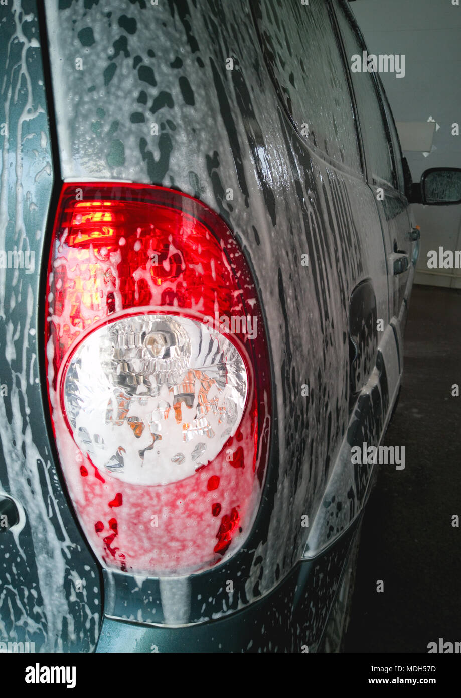 Car Wash. La schiuma gocciola verso il basso e si scioglie lo sporco sul corpo e sul retro del proiettore dell'auto. Foto Stock