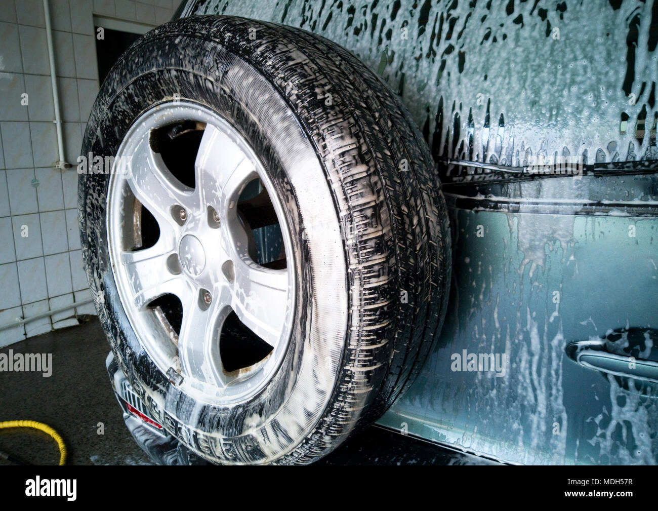 Car Wash. Schiuma drena verso il basso e si scioglie lo sporco sulla porta posteriore e ruota di scorta della vettura. Foto Stock