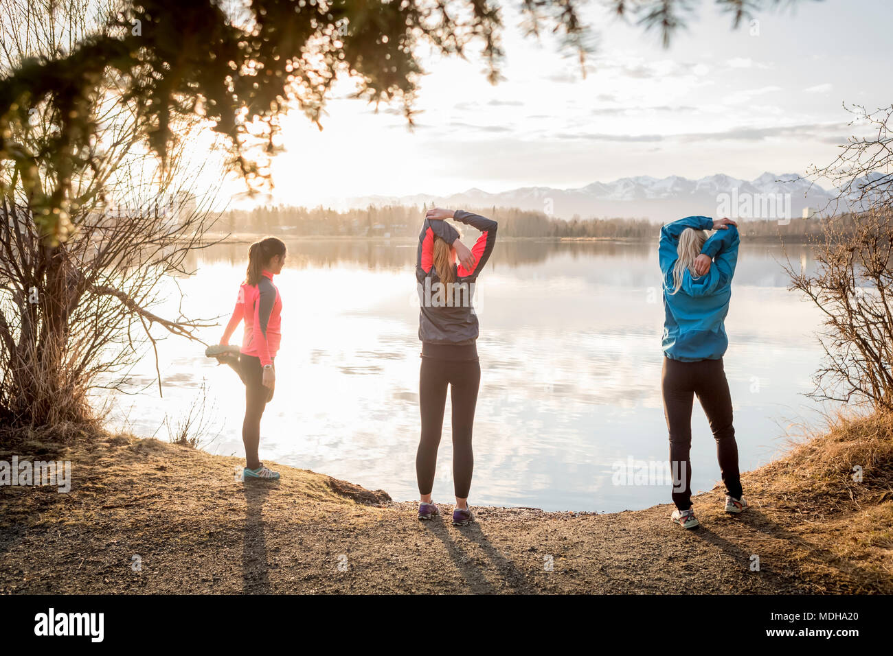 Tre giovani donne lo stiramento su un sentiero a bordo dell'acqua; Anchorage in Alaska,, Stati Uniti d'America Foto Stock