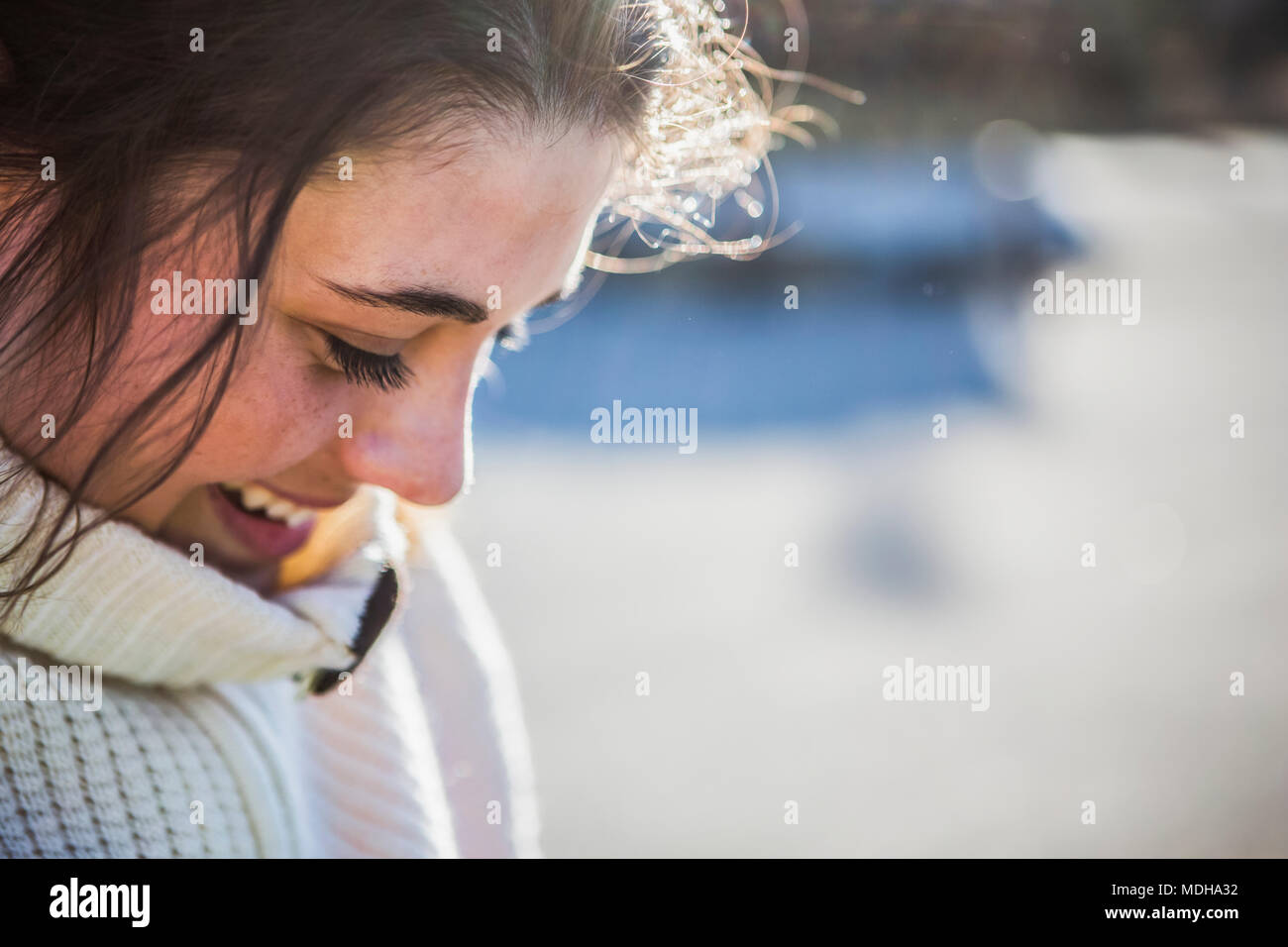 Una giovane donna con capelli castani guardando verso il basso e sorridente con i suoi capelli retroilluminati da luce solare; Anchorage in Alaska,, Stati Uniti d'America Foto Stock