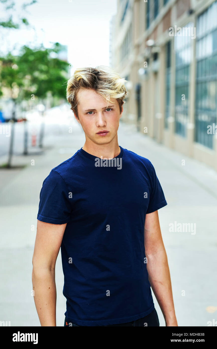 Ritratto di un ragazzo adolescente che indossa una maglietta blu e in piedi su un marciapiede in una zona urbana; Toronto, Ontario, Canada Foto Stock