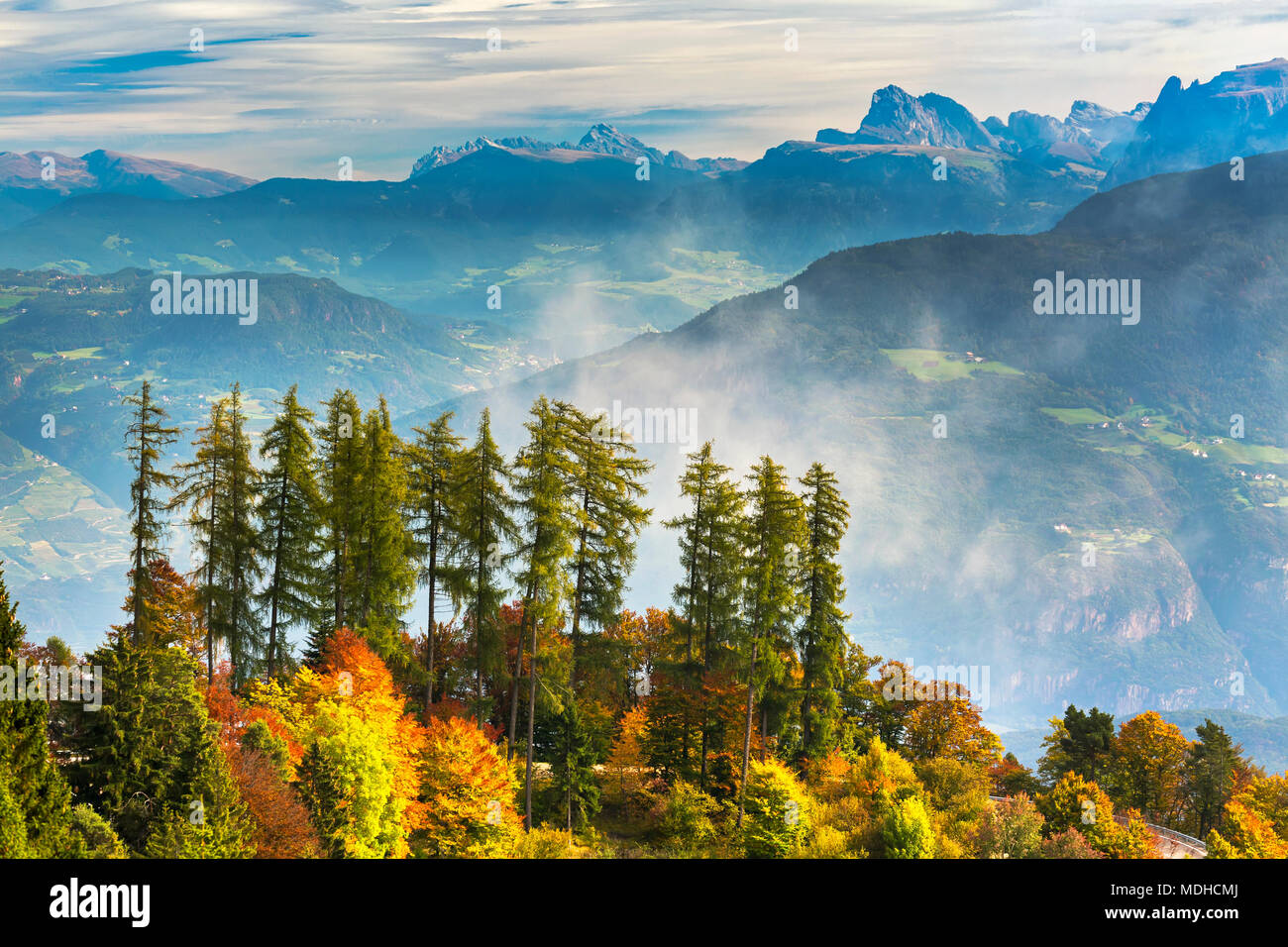 Alberi colorati in autunno su una cresta che domina la valle di rotolamento piste alpine e le montagne sullo sfondo con nebbia proveniente dalla valle Foto Stock