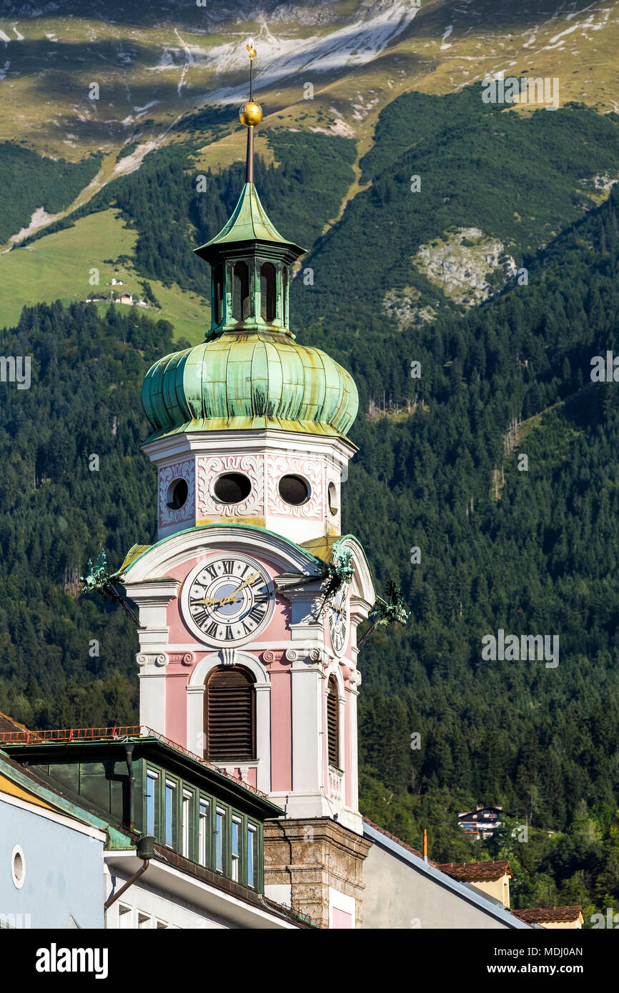 Chiesa decorativo torre dell orologio contro una alberata coperto pendio montano sfondo; Innsbruck in Tirolo, Austria Foto Stock