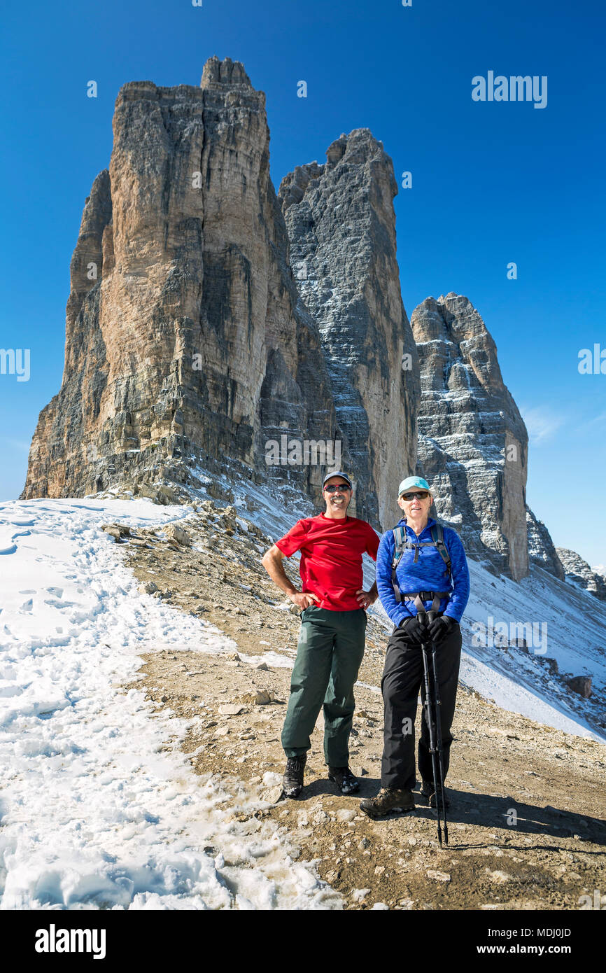 Maschio e femmina gli escursionisti in piedi sul pendio roccioso con spettacolari guglie di montagna e cielo blu; Sesto, Bolzano, Italia Foto Stock