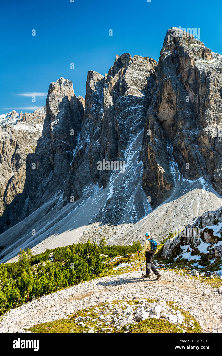 Escursionista femmina sul sentiero con la sottostante valle contro una robusta gamma di montagna e cielo blu; Sesto, Bolzano, Italia Foto Stock