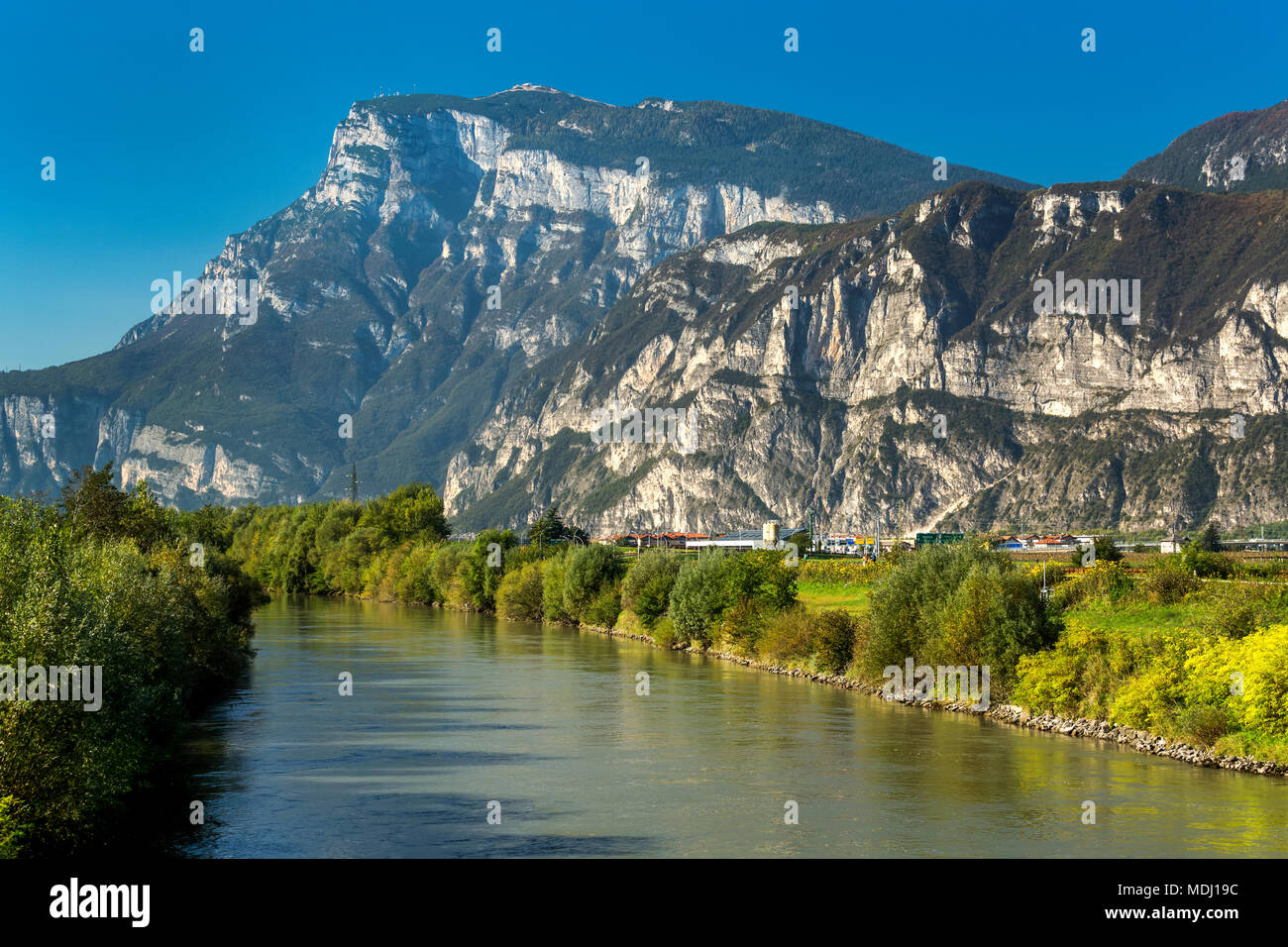Tranquillo fiume alberato Nel verde fogliame e aspre montagne sullo sfondo con cielo blu; Trento, Trento, Italia Foto Stock