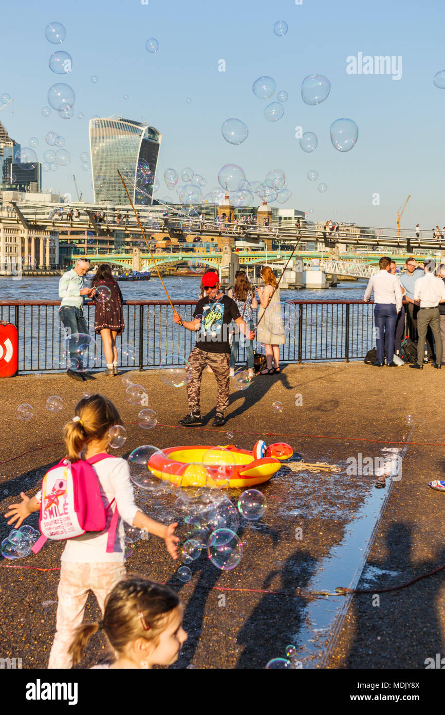 Londra, UK, 19 aprile 2018. Un intrattenitore sulla riva sud dell'argine del fiume Tamigi a Bankside soffia bolle per intrattenere i bambini contro un sfondo skyline iconica e moderno grattacielo edifici della città di Londra. La soleggiata bel tempo sul più caldo giorno di aprile in decenni portato fuori bonario folla per godersi il sole. Credito: Graham Prentice/Alamy Live News. Foto Stock