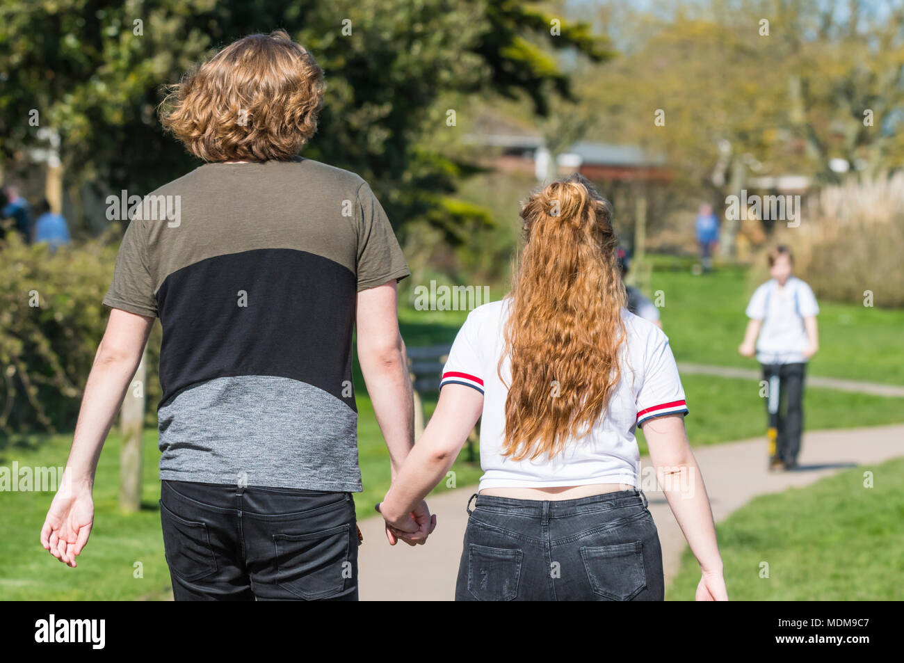 Coppia giovane holding hands parlando di una molla a piedi attraverso un parco su una calda giornata di primavera nel Regno Unito. Foto Stock