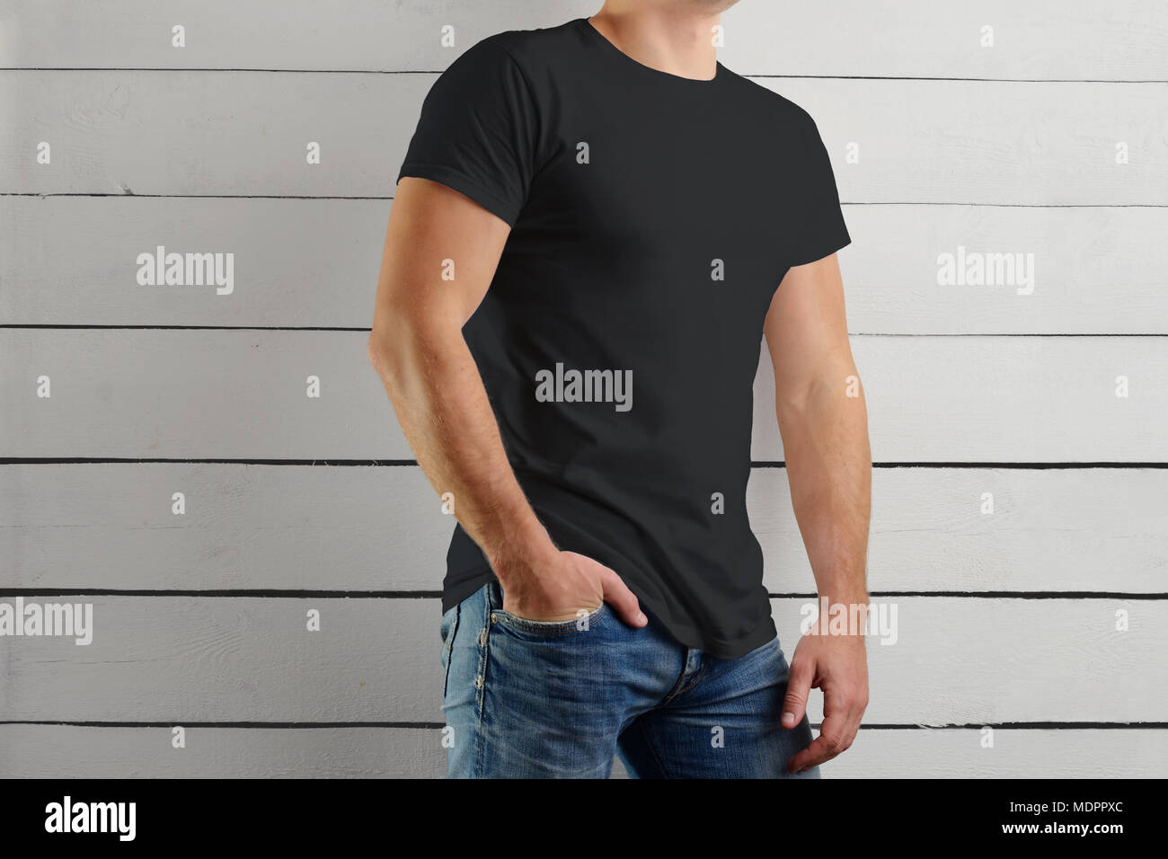 Mockup di una t-shirt nera su una forte guy standing è la metà di un giro su un sfondo di legno. Modello pronto per l'uso nella progettazione. Foto Stock